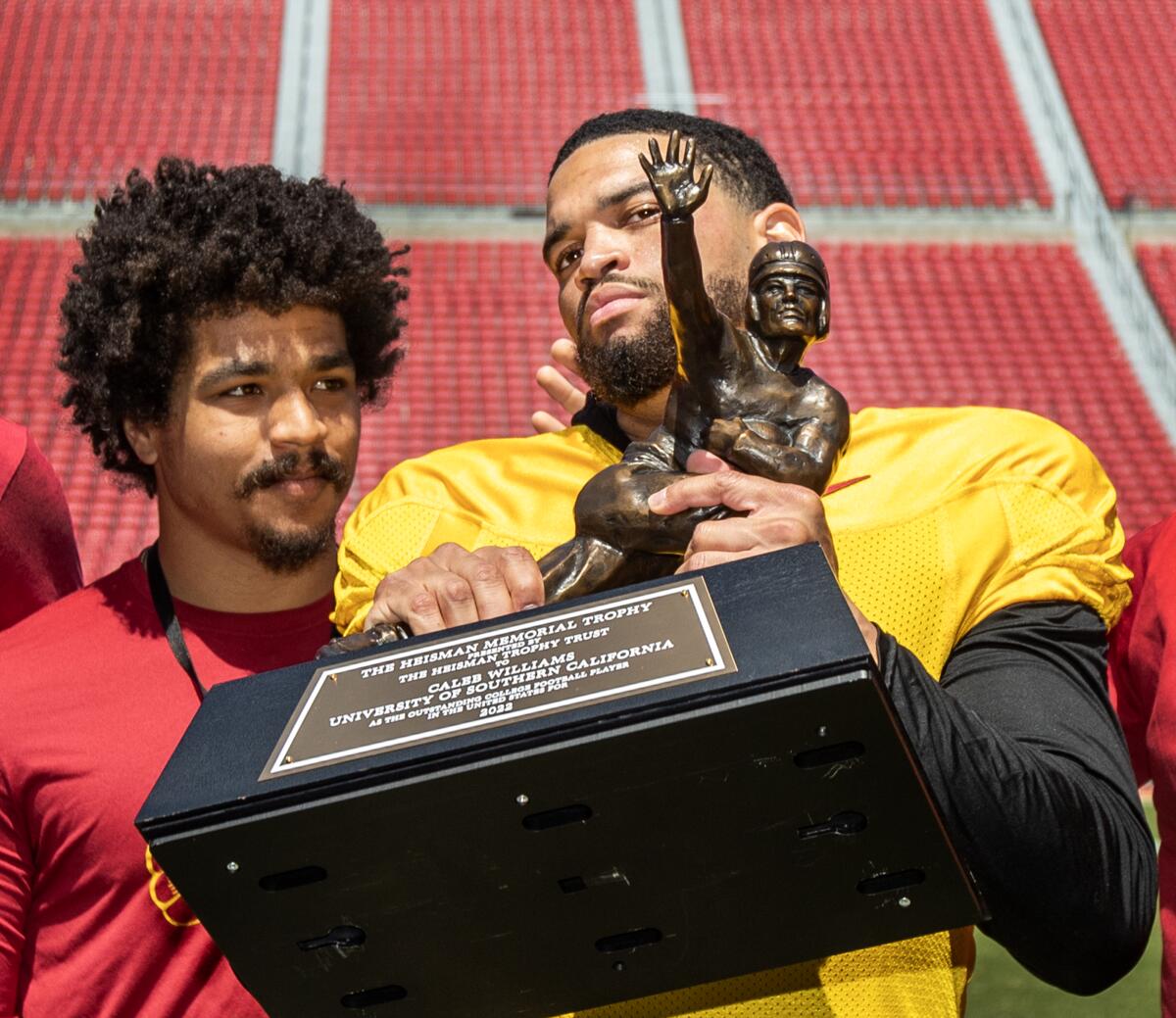 USC quarterback Caleb Williams shows off a replica of his Heisman Trophy in front of former Trojans running back Travis Dye.