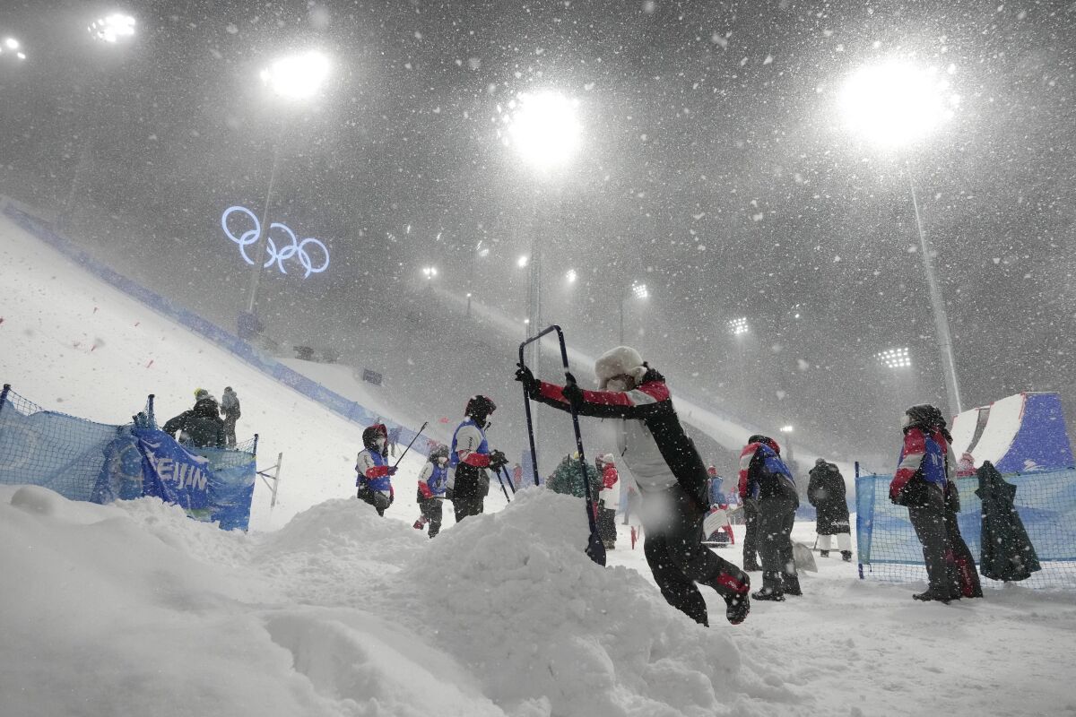 Volunteers clear the course as the women's aerials qualification has been delayed due to a weather condition at the 2022 Winter Olympics, Sunday, Feb. 13, 2022, in Zhangjiakou, China. (AP Photo/Lee Jin-man)