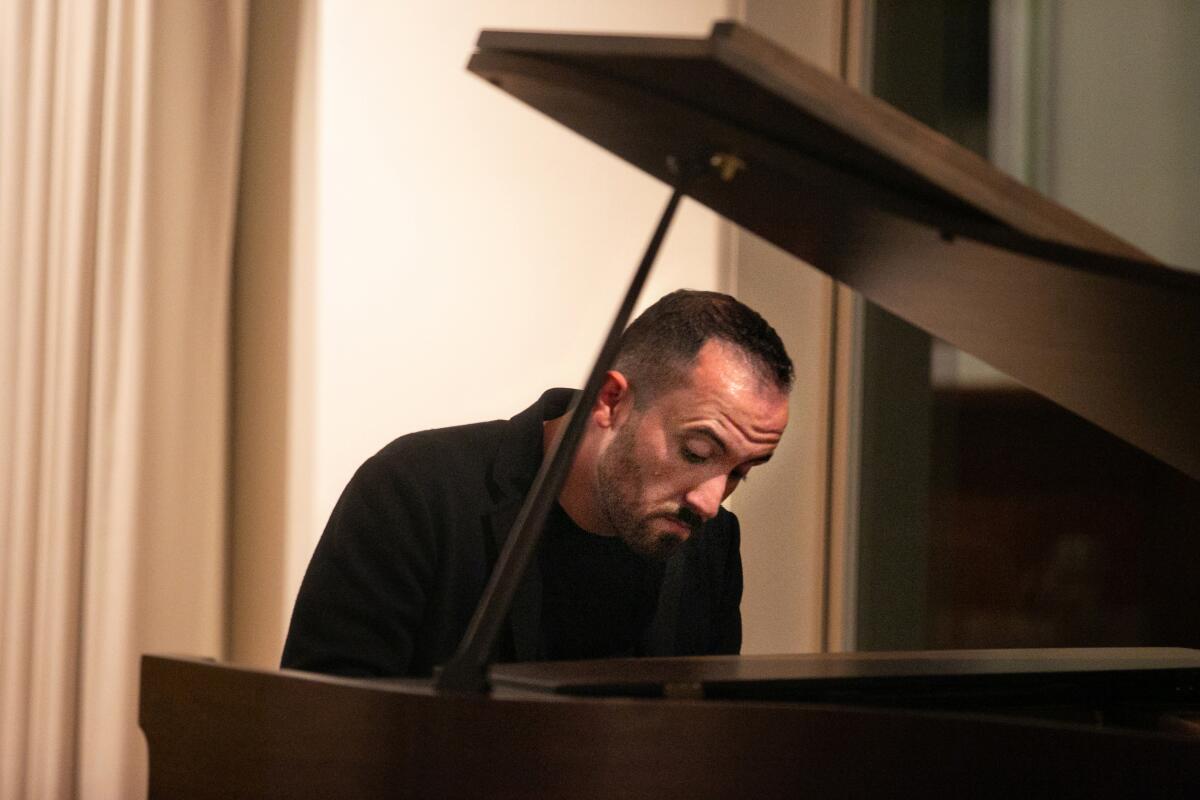 Igor Levit, wearing black, plays a black baby grand piano in a curtained room.