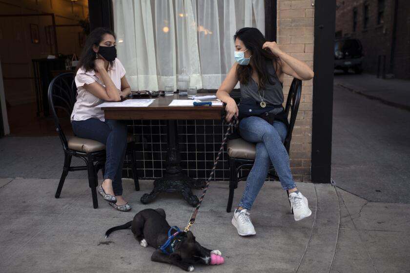PASADENA, CA - JULY 08: Sophia Desai, left, and Antia Yang, right, and her dog "Asha Blue" enjoy dinner at Perle Resteraunt Wednesday, July 8, 2020 in Pasadena, CA. Perle Resteraunt is a new French resteraunt that just opened in Pasadena. They are doing take out and have a few tables outside their front door. (Francine Orr / Los Angeles Times)