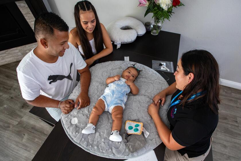 Cudahy, CA - August 23: Parent coach Alba Mariscal, right, is making a home visit on Wednesday, Aug. 23, 2023, in Cudahy, CA. She is checking in with father Chayanne Nino, left, mother Daniela Prada, middle, and their four-month-old infant daughter Salome Nino. Parent coaches go house to house, checking in on these families through the first year of their baby's life. They offer tips and advice, and often just support in what is often a very challenging (though exciting) moment for new parents. But funding for this crucial program is at risk. First 5 is funded through a tobacco tax, and as more and more Californians give up their cigarettes, that funding money is starting to dry up. (Francine Orr / Los Angeles Times)