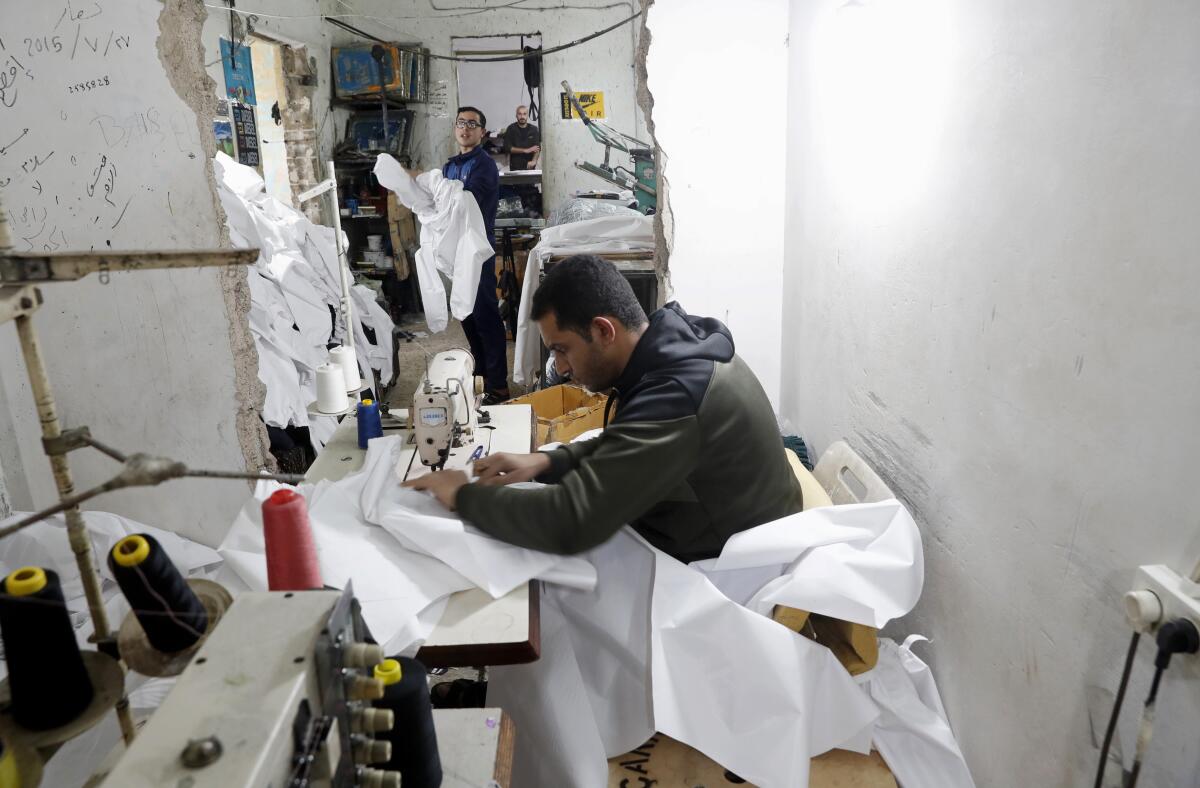FLE - In this Monday, March 30, 2020 file photo, Palestinians make protective overalls meant to shield people from the coronavirus, to be exported to Israel, at a local factory, in Gaza City. For the first time in years, some sewing factories in the Gaza Strip are back to working at full capacity — producing masks, gloves and protective gowns, some of which are bound for Israel.(AP Photo/Adel Hana, File)