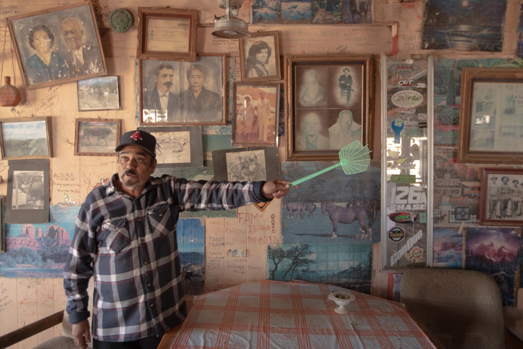 A man holding a fly swatter, in front of a wall covered in old family photos.