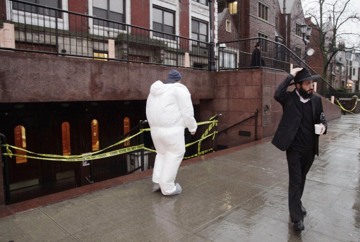 A crime scene investigator, center, passes a member of the Lubavitch community as he enters Chabad-Lubavitch Hasidic headquarters Tuesday.