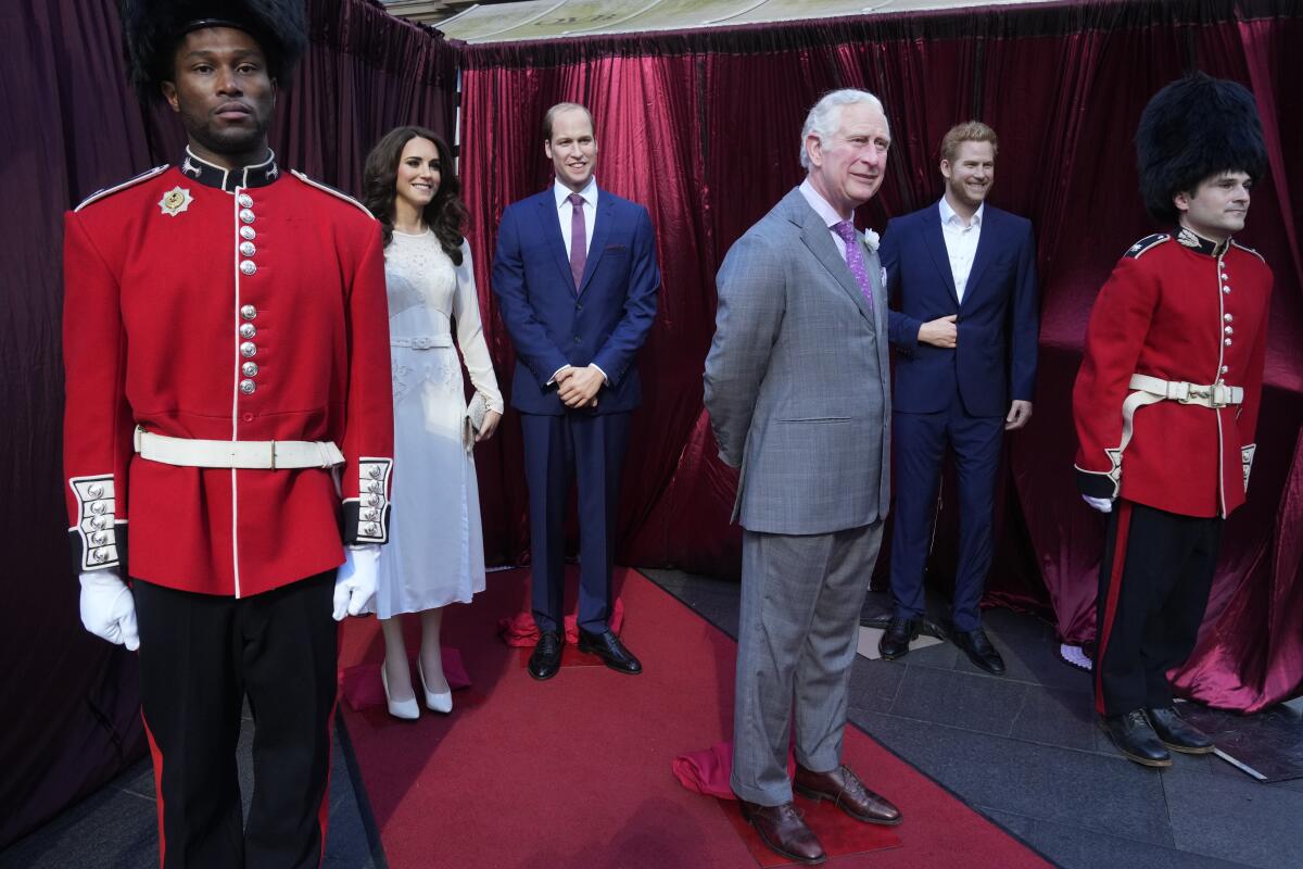Men dressed as royal guards stand watch over wax figures King Charles III, Prince William, Kate and Prince Harry.