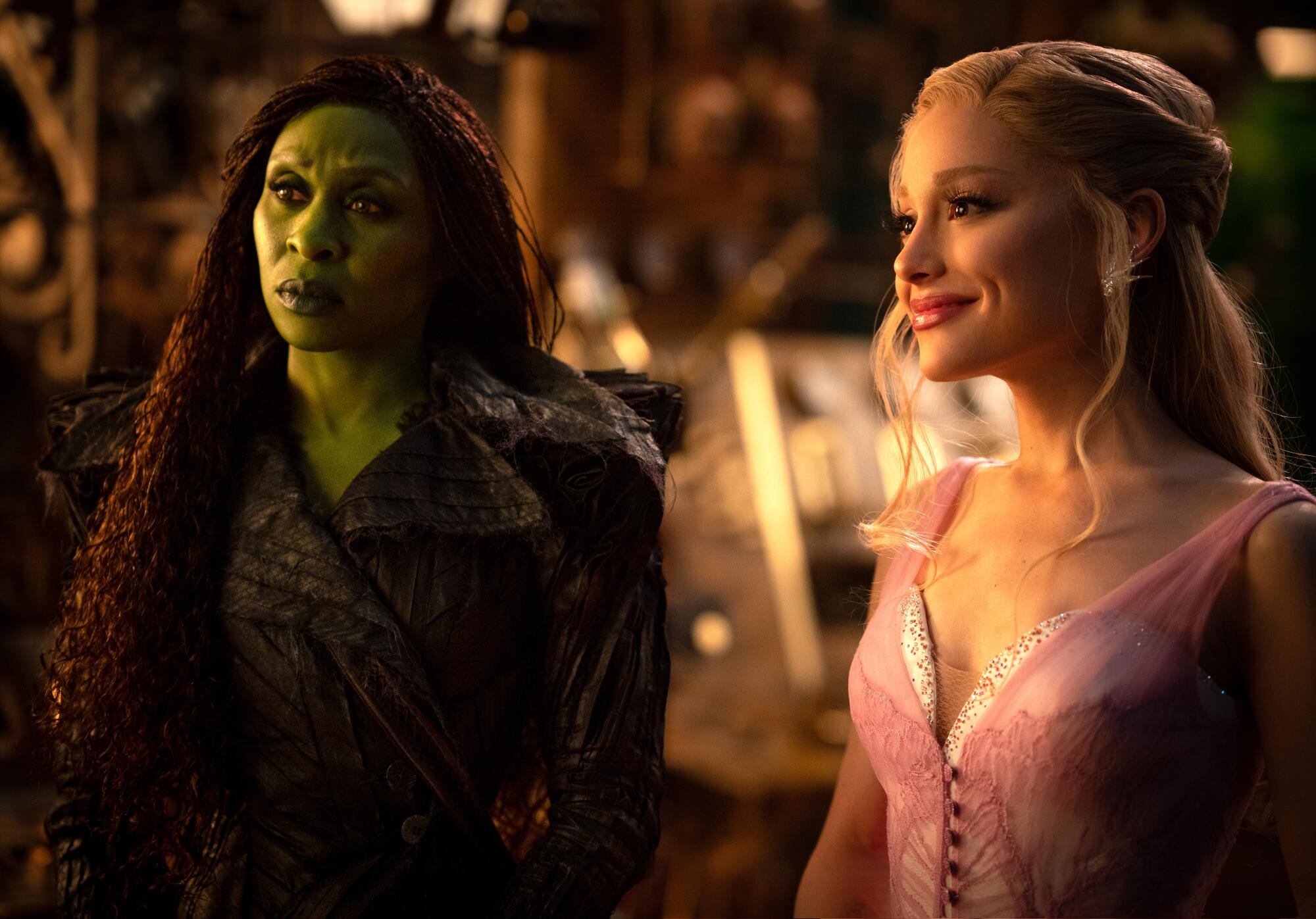 A green-skinned witch and another witch in a pink dress stand next to each other.