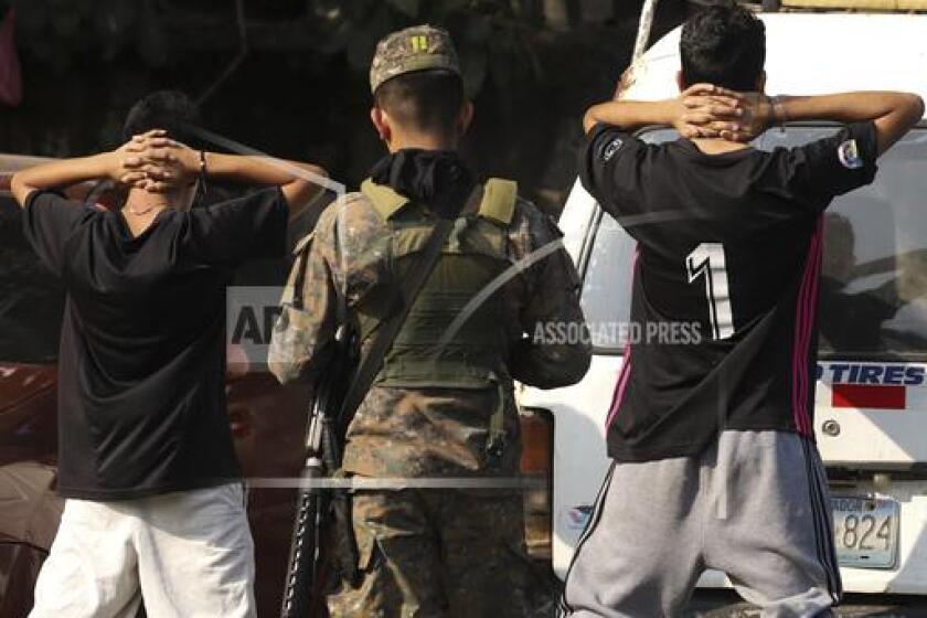 Un militar comprueba la identidad de dos jóvenes en plena calle en el barrio de La Campanera en Soyapango, El Salvador, el domingo 5 de marzo de 2023. Enn La Campanera, en su momento uno de los vecindarios más sangrientos del país, la policía y los soldados piden a los hombres que se quiten las camisetas para verificar si tienen tatuajes en busca de evidencias de que no son parte de la banda Barrio 18, que dominaba allí. La CIDH pidió a El Salvador el miércoles 12 de abril de 2023 que restablezca los derechos suspendidos. (AP Foto/Salvador Melendez)