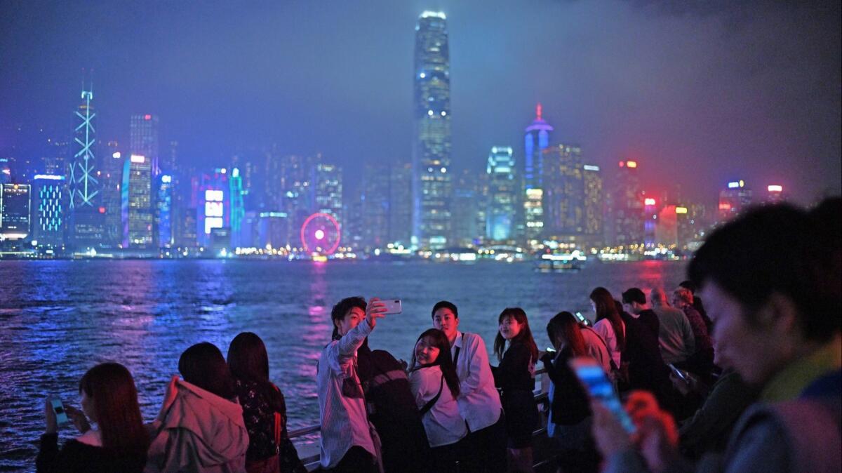 Friends pose for a selfie near the Kowloon Star Ferry pier, the Hong Kong skyline as their backdrop.