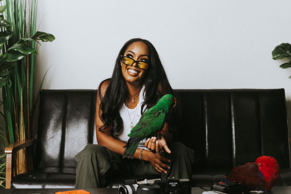 Photographer Delaney George sits casually on a couch with a parrot on her arm.