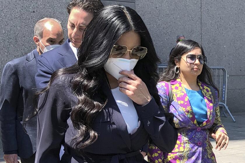 A woman with long black hair walking while wearing a white face mask and sunglasses