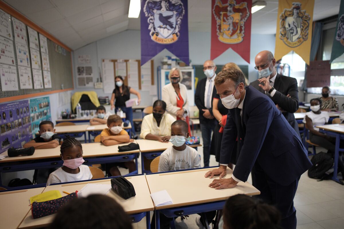 French President Emmanuel Macron, center, flanked with French Education, Youth and Sports Minister Jean-Michel Blanquer, right, speaks with children during a visit at Bouge primary school in Malpasse district of Marseille, southern France, Thursday Sept. 2, 2021 as twelve million children in France went back to school Thursday for the new academic year, wearing face masks as part of rules aimed at slowing down the spreading of the virus in the country. French President Emmanuel Macron, accompanied by several ministers, is on a three-day visit to the southern city of Marseille to address security, education and housing issues. (AP Photo/Daniel Cole, pool)