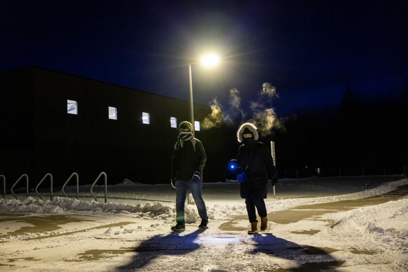 AMES, IOWA - JANUARY 15, 2024: Condensation forms as Natalia Porter, right, of Huntington Beach and her son-in-law Jonathan Stoner breath the sub-zero air on a snowy path to Caucuses night at Mitchell Elementary School on January 15, 2024 in Ames, Iowa. Porter is going to observe the process while Stoner, originally from Lakewood, California and now living in Ames, Iowa will be voting. (Gina Ferazzi / Los Angeles Times)