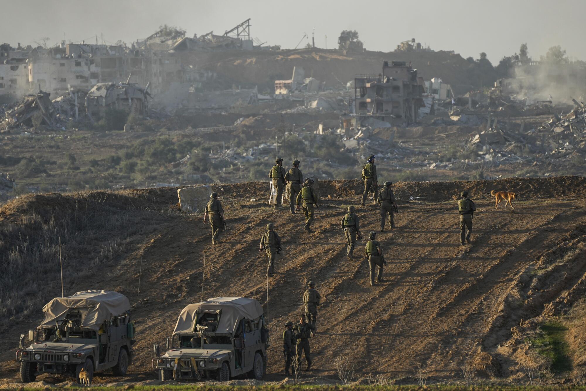 Israeli troops walk near vehicles.