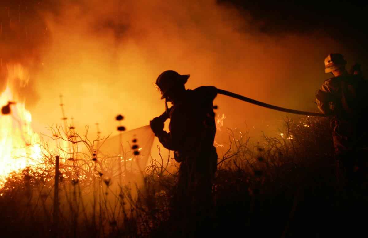 A firefighter hoses down flames spread by Santa Ana winds in 2007.
