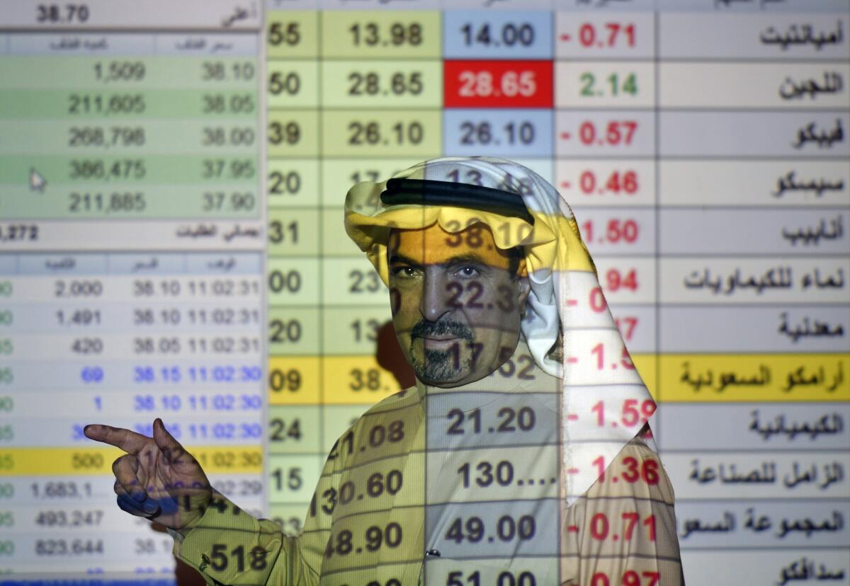FILE- In this Dec. 12, 2019, file photo, a trader talks to others in front of a screen displaying Saudi stock market values at the Arab National Bank in Riyadh, Saudi Arabia. Saudi Aramco said Tuesday, May 4, 2021, it's profits soared by 30% for the first-quarter of the year, compared to last year, riding on the back of higher crude oil prices as some of the world's biggest economies claw their way out of recession and ease restrictions amid vaccine roll-outs against COVID-19.(AP Photo/Amr Nabil, File)