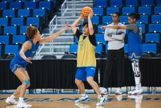Oscar Dela Cruz holds up the ball and is guarded by guard Kiki Rice during a UCLA women's basketball practice.