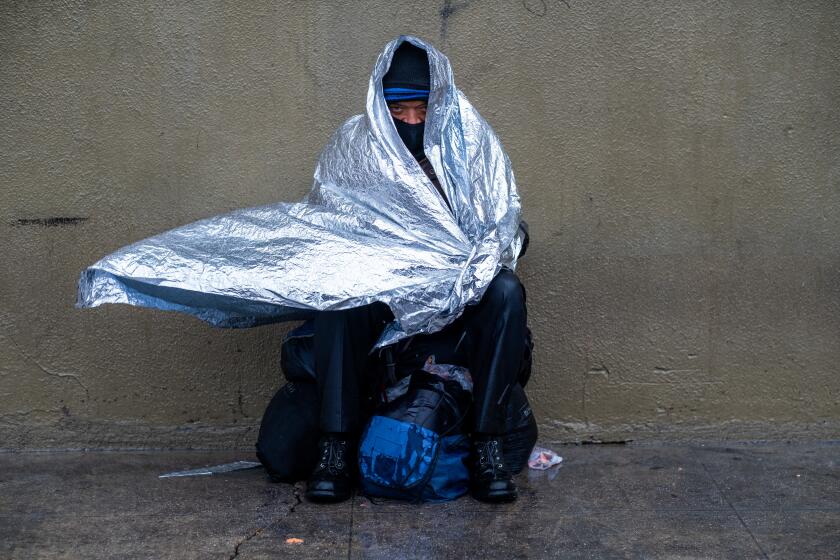 Los Angeles, CA - February 24: It's raining, cold, and windy Maurice, age 50, sits outside Fred Jordan Mission in skid row trying to stay warm on Friday, Feb. 24, 2023, in Los Angeles, CA. (Francine Orr / Los Angeles Times)