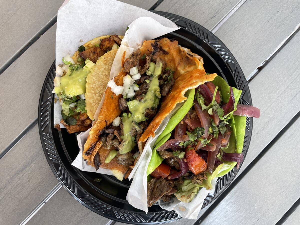 Three tacos side by side on a black plate