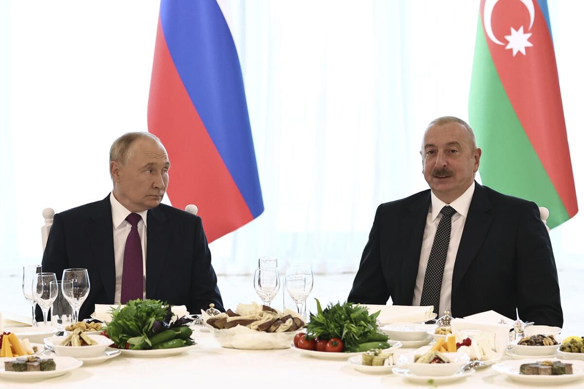 Vladimir Putin, left, and Ilham Aliyev sit at a table set for a meal in front of flags