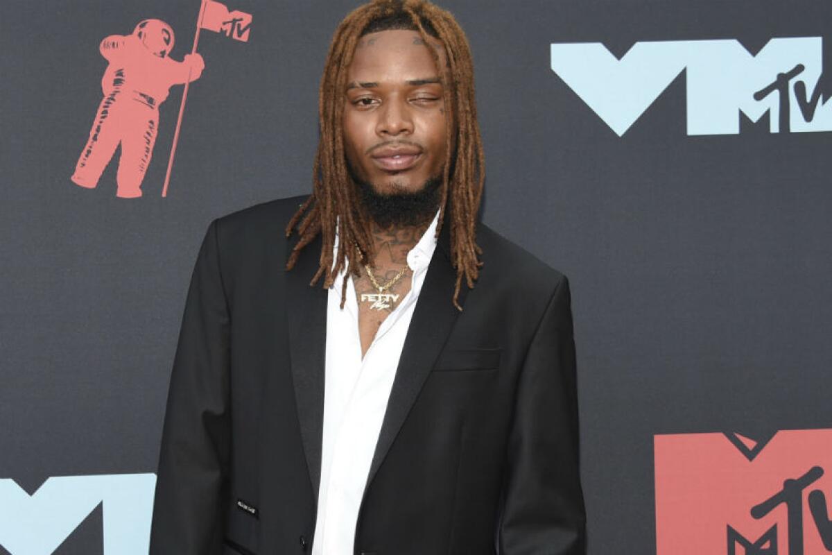 A man in a dark suit and white shirt stands in front of an MTV-branded backdrop.