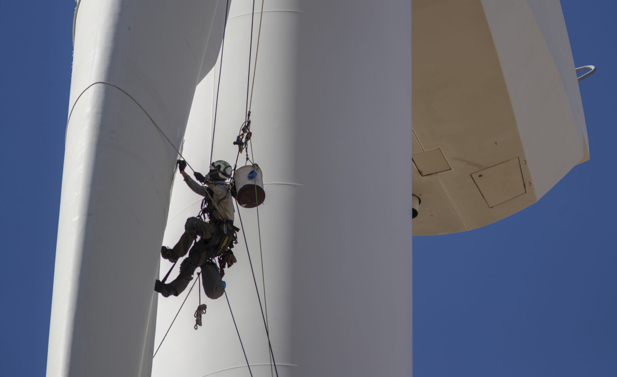 A person hangs from a winde turbine.