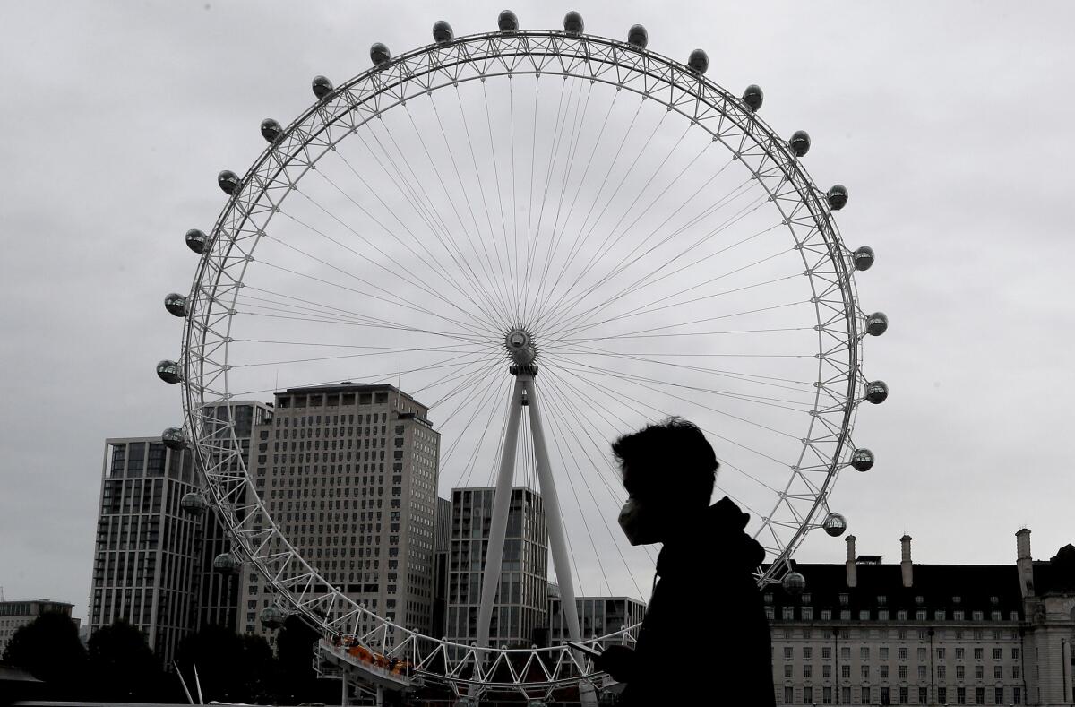 Una persona con cubrebocas camina frente al London Eye en Londres.