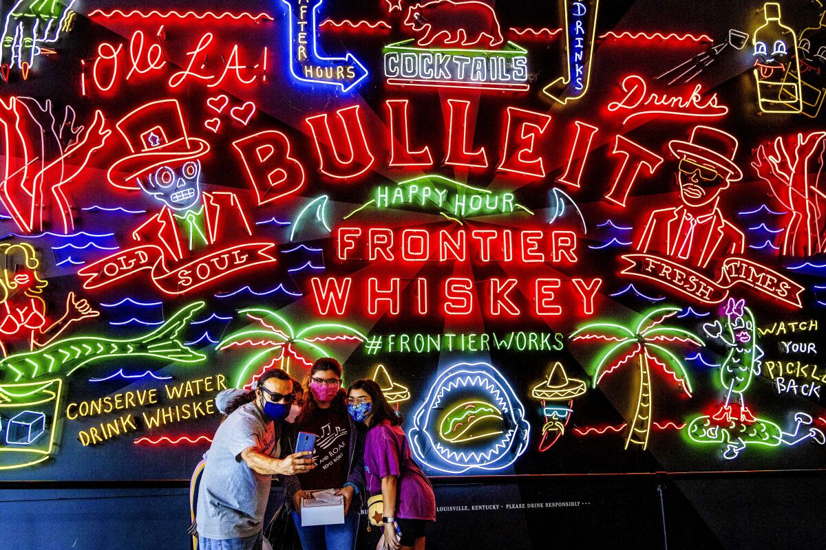 A group takes a selfie in front of the neon BULLEIT sign inside Grand Central Market in downtown Los Angeles.