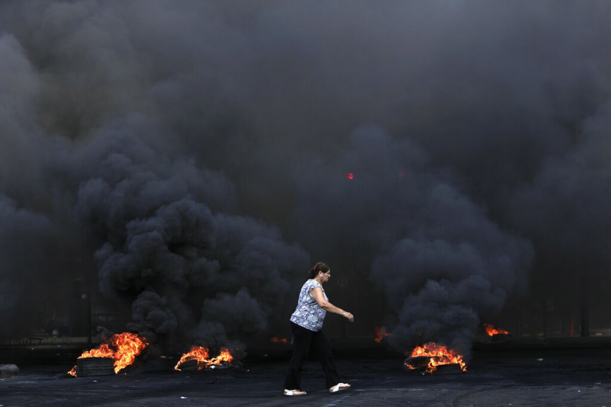A woman walks past burning tires that were used to block a road during a protest in Beirut on Friday.