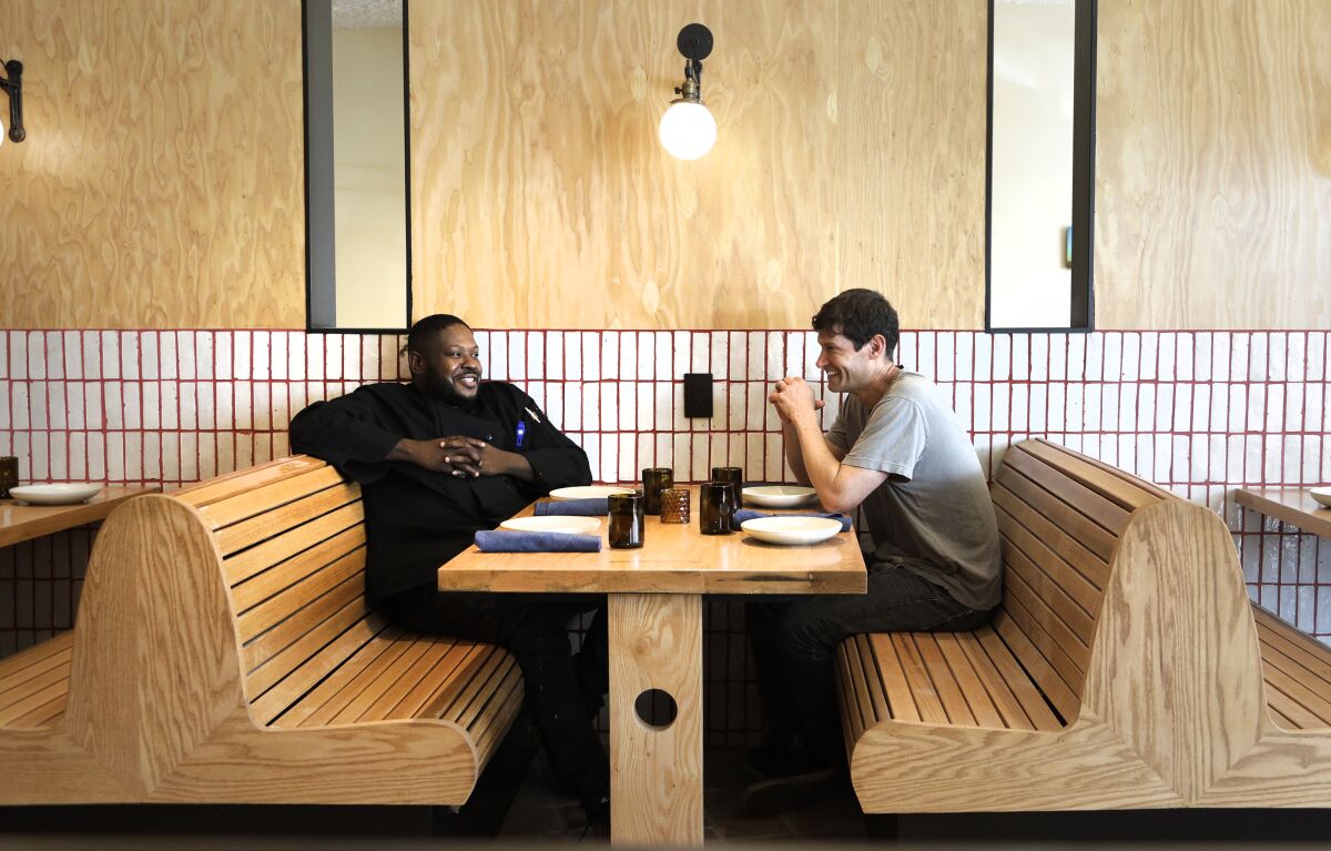 Two men sit in a restaurant booth smiling and talking 