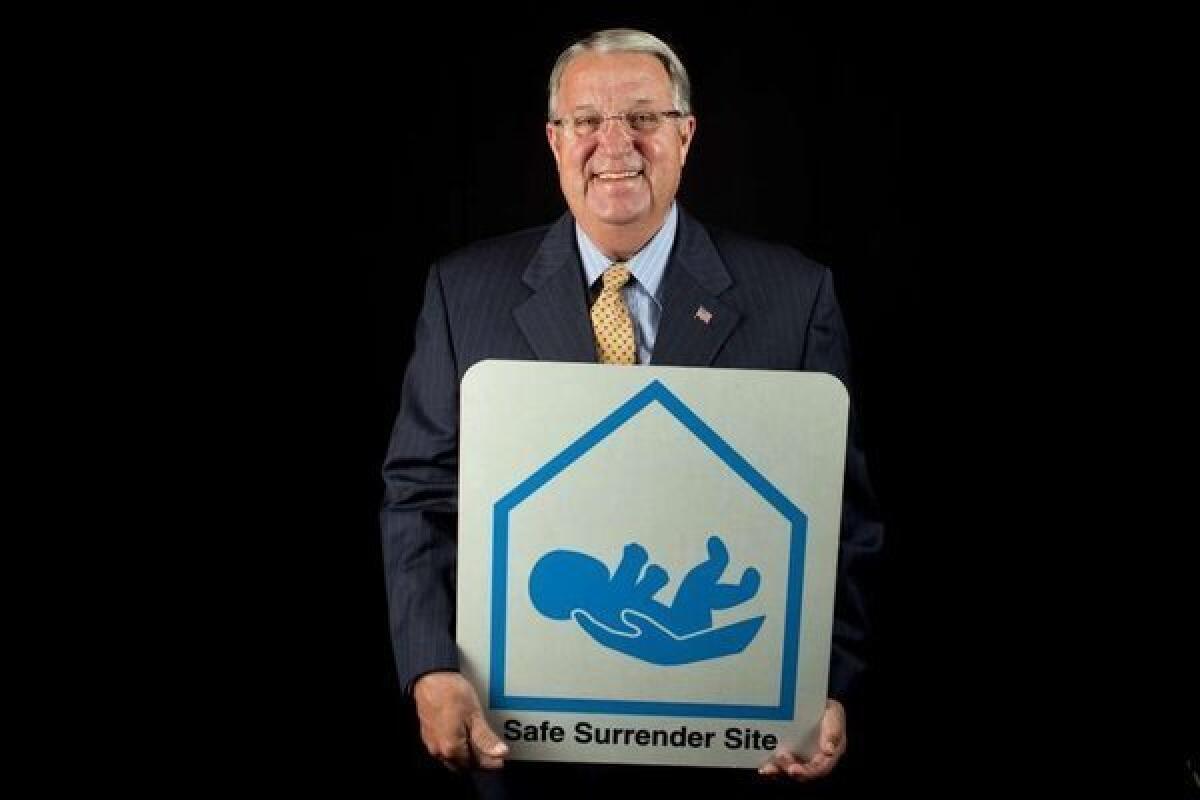 L.A. County Supervisor Don Knabe, holding a sign from his proudest accomplishment, the "safe surrender" program for saving newborns, which just reached the 100-baby mark. A new report asks questions again about Knabe and his lobbyist-son's clients' business with L.A. County.
