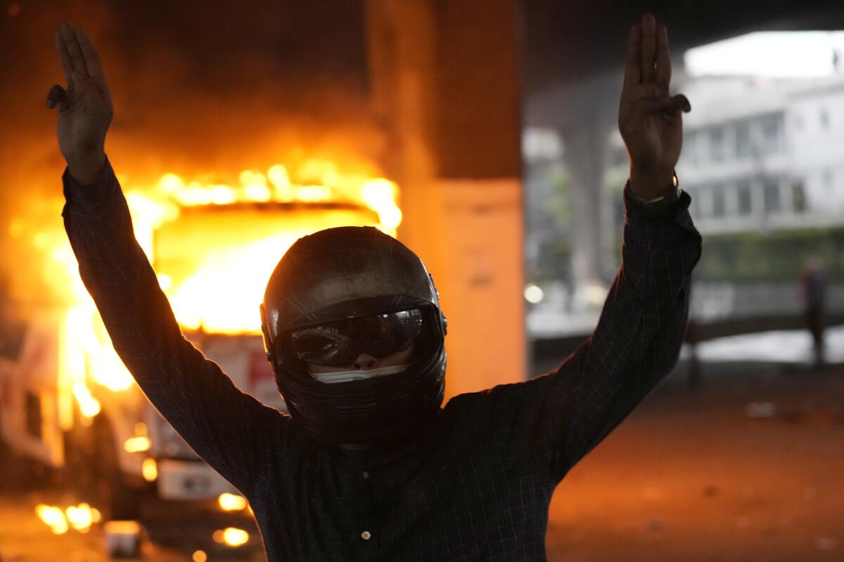 Anti-government protester display the three-finger symbol of resistance in front of burning police truck during protest in Bangkok, Thailand, Wednesday, Aug. 11, 2021. Protesters demanded the resignation of Prime Minister Prayuth Chan-ocha for what they say is his failure in handling the COVID-19 pandemic. (AP Photo/Sakchai Lalit)