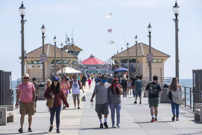 People walk along the Huntington Beach Pier after it opened mid day for the first time in months on Tuesday, May 26.