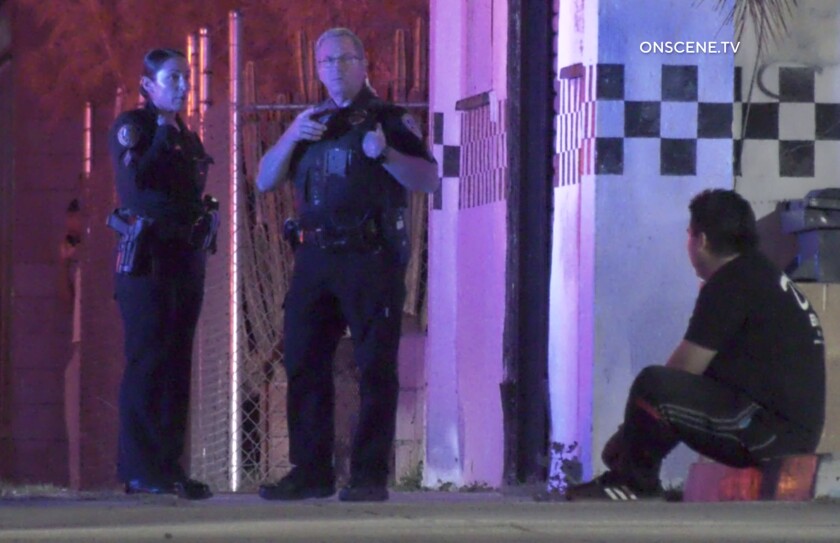 Two uniformed police officers stand near a seated man.