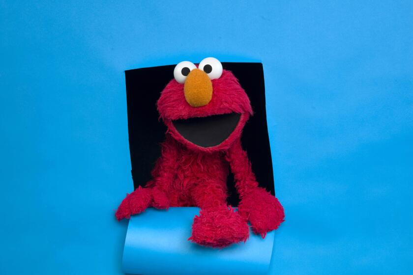 A red Elmo puppet posing against a blue background