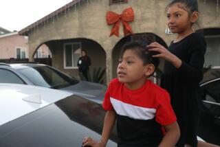 Boyle Heights, CA - December 13: Matthew Rodriguez, 3, left, and Alison Rodriguez, 7, right, play on top of a car as their mom Perla Ortega looks in the background on Wednesday, Dec. 13, 2023 in Boyle Heights, CA. (Michael Blackshire / Los Angeles Times)
