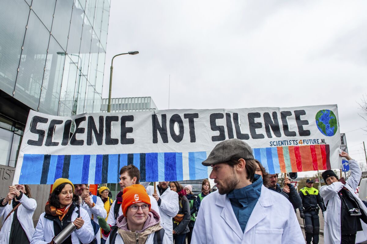Scientists wearing lab coats protesting with a sign that reads "Science not silence" 