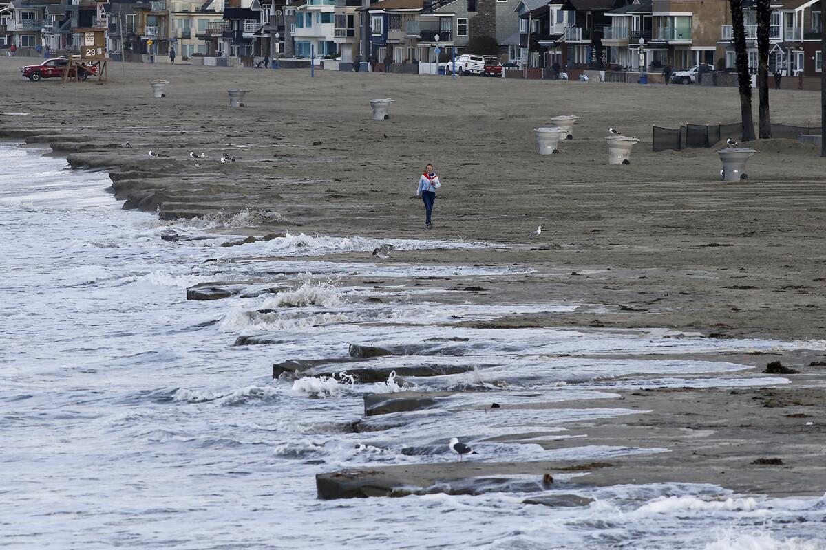 High tide pushes back the coastline as a woman walks along north side of Newport Beach Pier on Friday.
