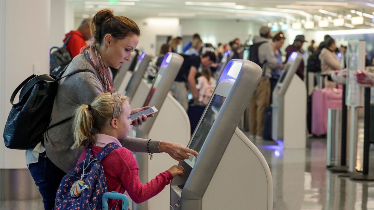 Katy Von Treskow, left, traveling with her 5-year-old daughter, Madeline, uses a check-in kiosk at Los Angeles International Airport. A study found the surfaces of such kiosks are high in bacteria.