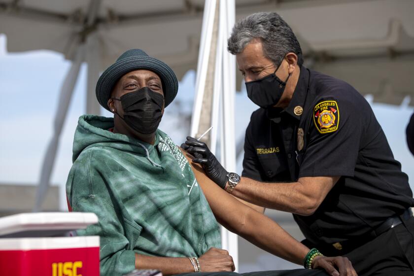 LOS ANGELES, CA - MARCH 24, 2021: Los Angeles Fire Chief Ralph Terrazas gives a vaccine shot to Arsenio Hall on the rooftop of parking structure at USC as a part of a vaccination awareness event at USC on March 24, 2021 in Los Angeles, California.(Gina Ferazzi / Los Angeles Times)