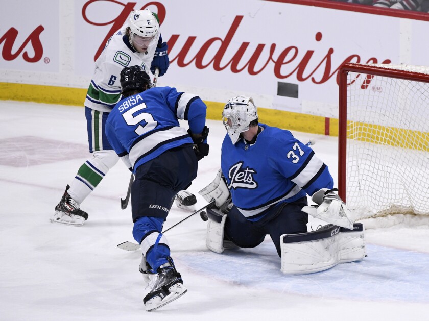 Winnipeg Jets goaltender Connor Hellebuyck (37) makes a save on Vancouver Canucks' Brock Boeser (6) as Luca Sbisa (5) defends during the third period of an NHL hockey game Tuesday, Jan. 14, 2020, in Winnipeg, Manitoba. (Fred Greenslade/The Canadian Press via AP)