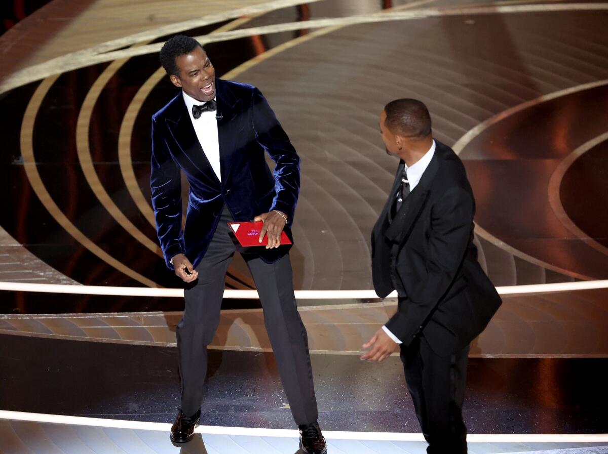 two men in tuxes on a stage, one reacting to the other