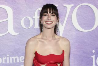 Anne Hathaway smiling in a strapless red dress and dangly earrings with her long dark hair pulled back from her face