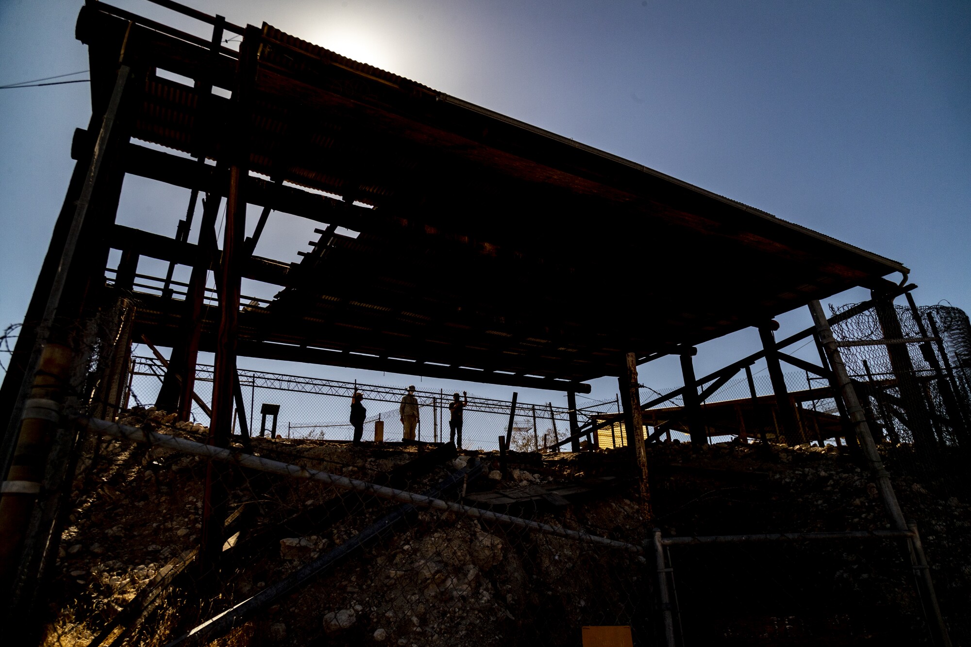 Three people stand under a tall roof of corrugated panels over an excavation pit