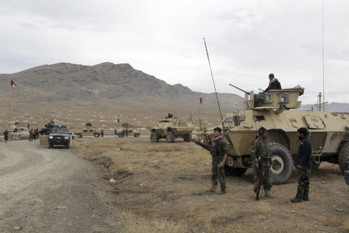 Armored vehicles are lined up, and Afghan soldiers carry weapons at the site of a suicide bombing.