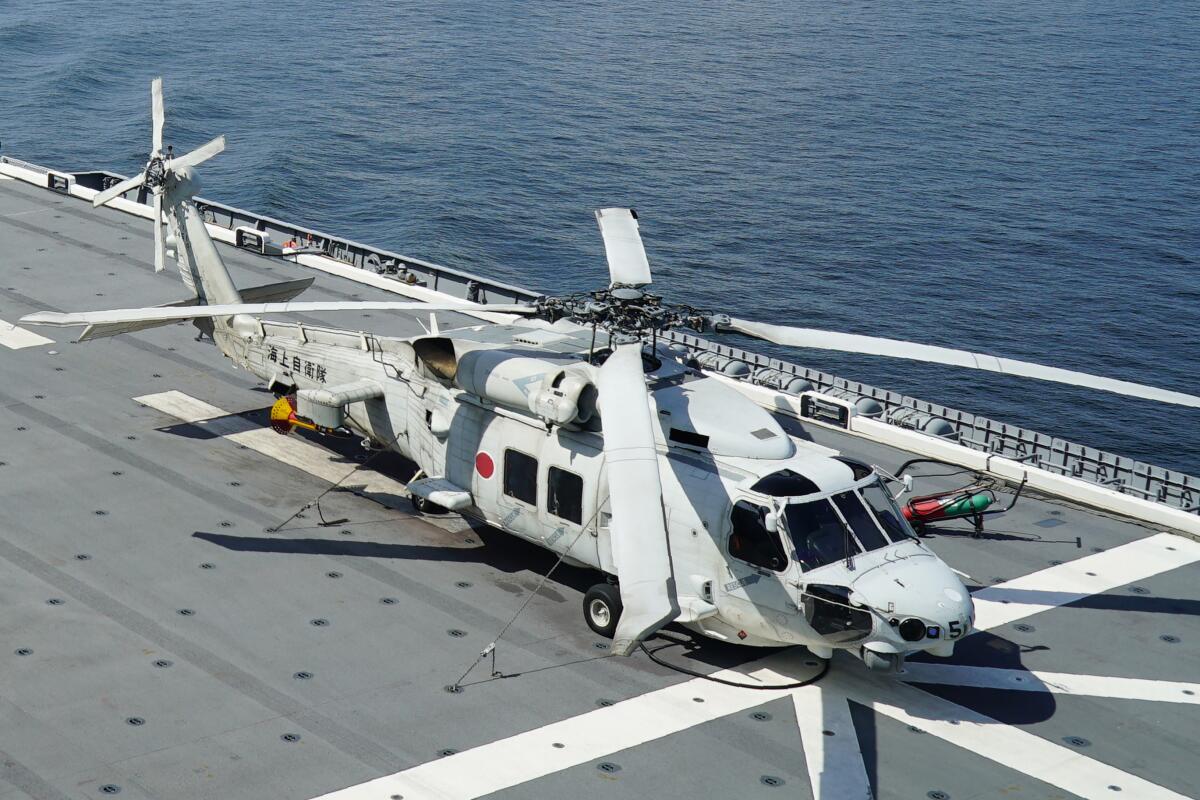 A white helicopter at rest on the deck of an aircraft carrier, the ocean visible below