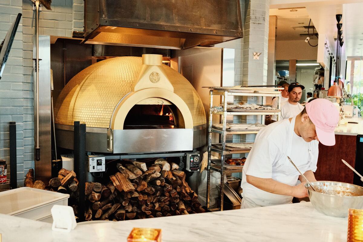 A staff member preps items near the shiny gold-tiled pizza oven seen at the entrance of Leopardo restaurant on La Brea