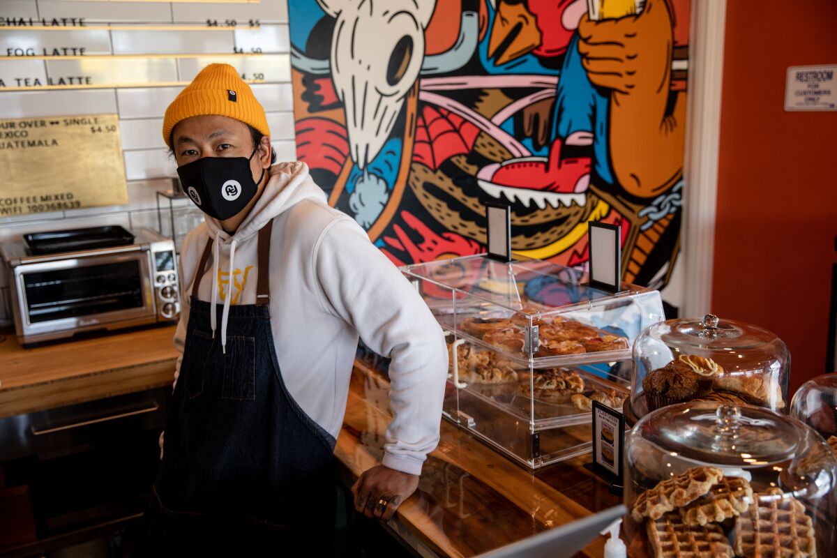 Kwa Nguyen, co-owner of Mixed Grounds coffee shop, stands near artwork in the store Thursday.