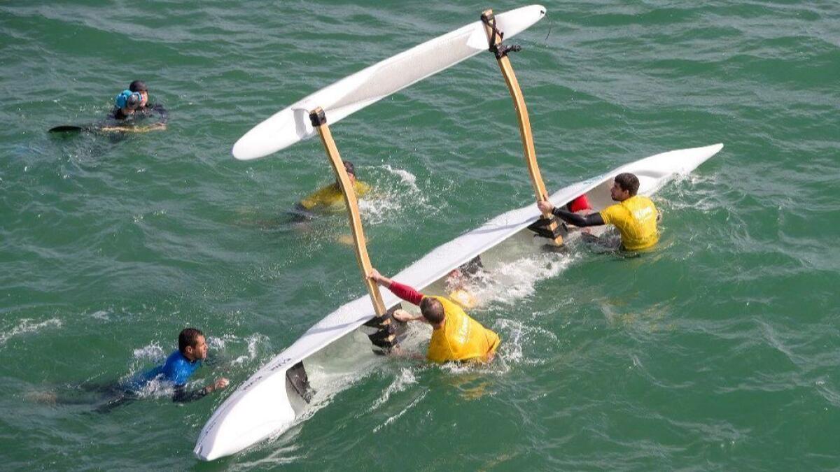 A four-man crew flips an outrigger surf canoe to purge the water from it Friday near the Huntington Beach Pier.