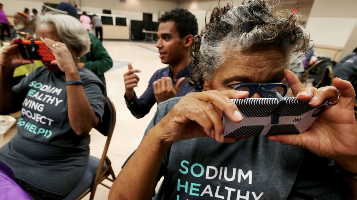 Technician Ryan Anderson, center, helps Sodium Healthy Living Project participants Sandra Goldsmith, 74, left, and Blanche Ross, 83, use their mobile phones to view a virtual reality video telling them about different foods and their sodium content.