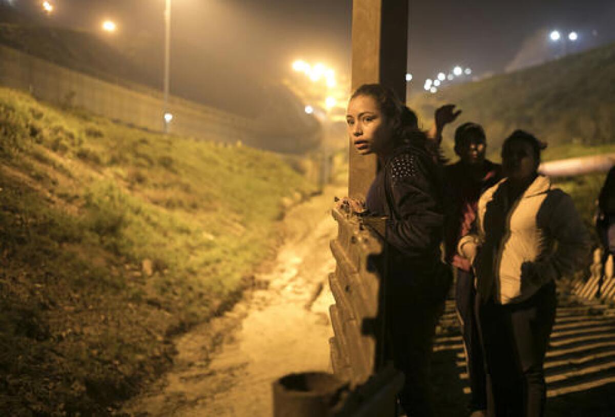 En esta imagen del 8 de febrero de 2019, la adolescente salvadoreña Xiomara Henríquez Ayala mira a la cerca fronteriza que separa Estados Unidos de Tijuana, México, buscando una forma para ayudar a sus acompañantes a cruzar sin ser detectados. (AP Foto/Emilio Espejel, archivo)